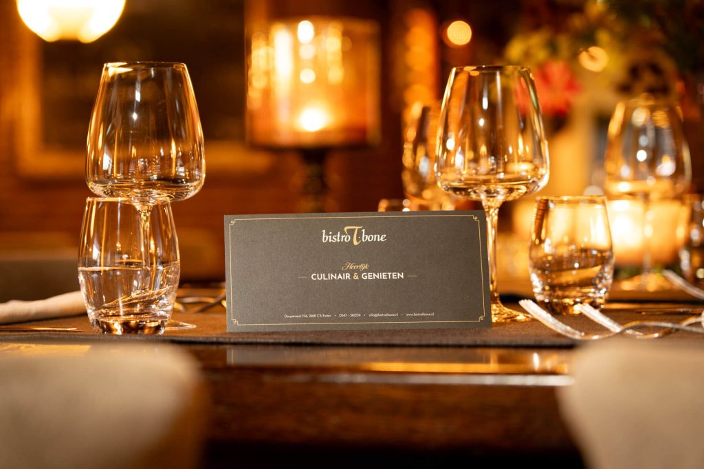 Geschenkbon van Bistro T-Bone op sfeervol gedekte restauranttafel met wijnglazen en warm kaarslicht