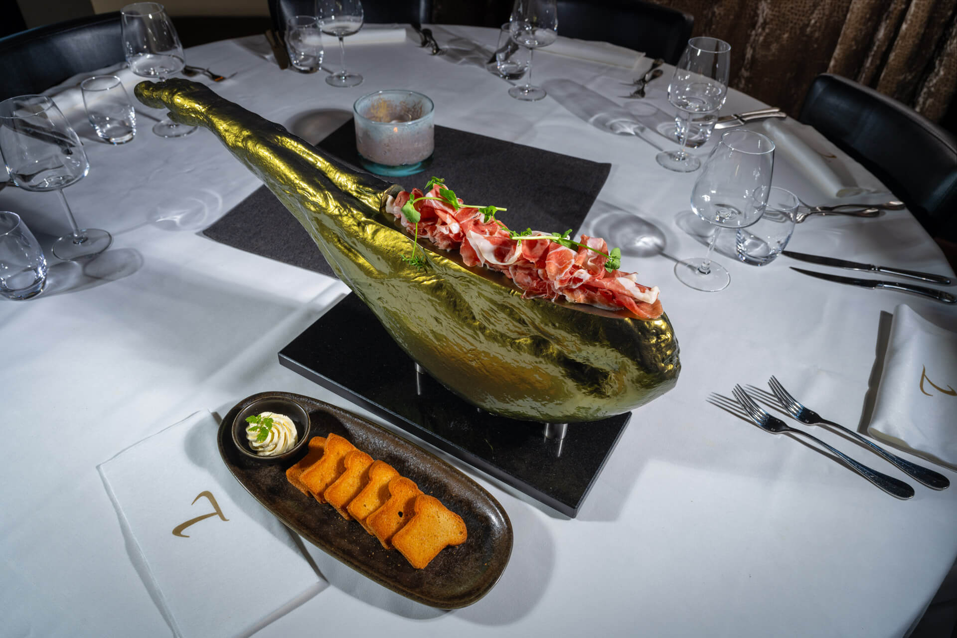 Pata Negra ham geserveerd in gouden hamhouder met krokante toast en crème op tafel bij Bistro T-Bone